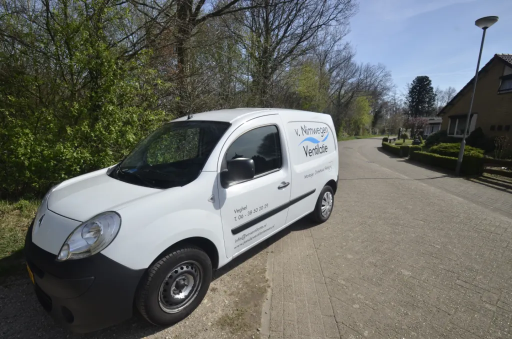 Witte bestelbus met de belettering van v. Nimwegen Ventilatie, geparkeerd langs een klinkerstraat in een woonwijk met bomen