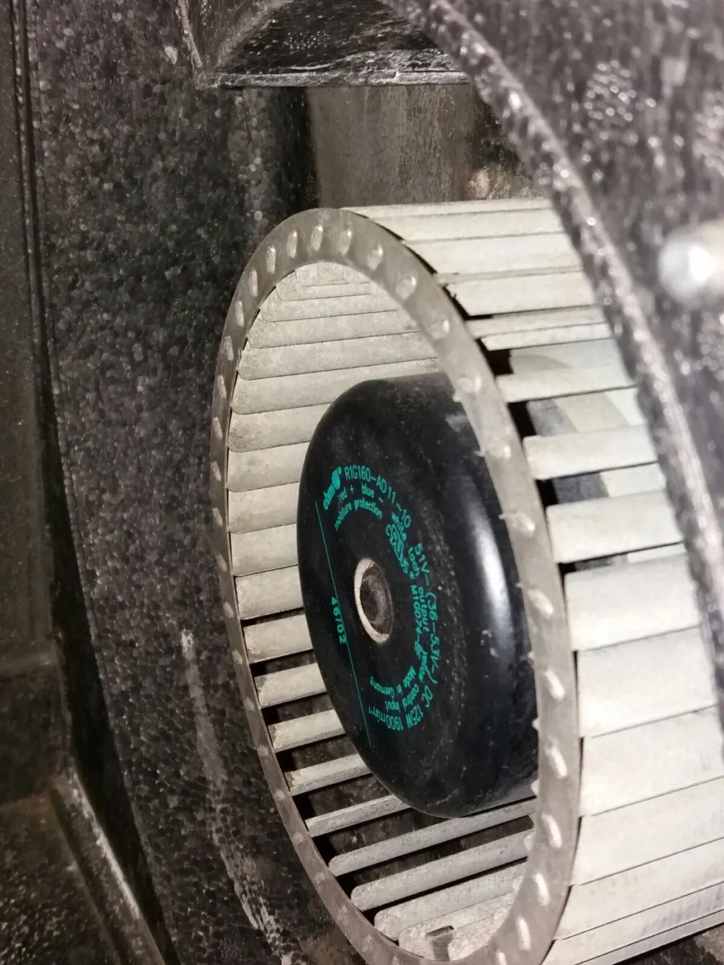 Ventilatorwiel met de motor in het midden, in de behuizing van een ventilatie-unit; op de schoepen en de wanden ligt stof